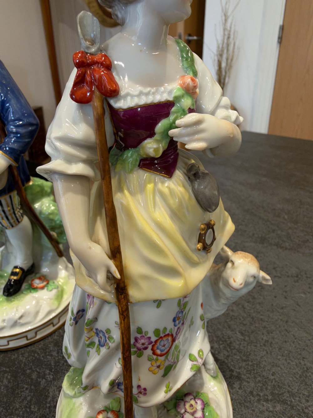 A pair of antique hand-painted German porcelain figures depicting a shepherdess with a lamb and a shepherd holding a basket, set on circular gilded bases. View XII