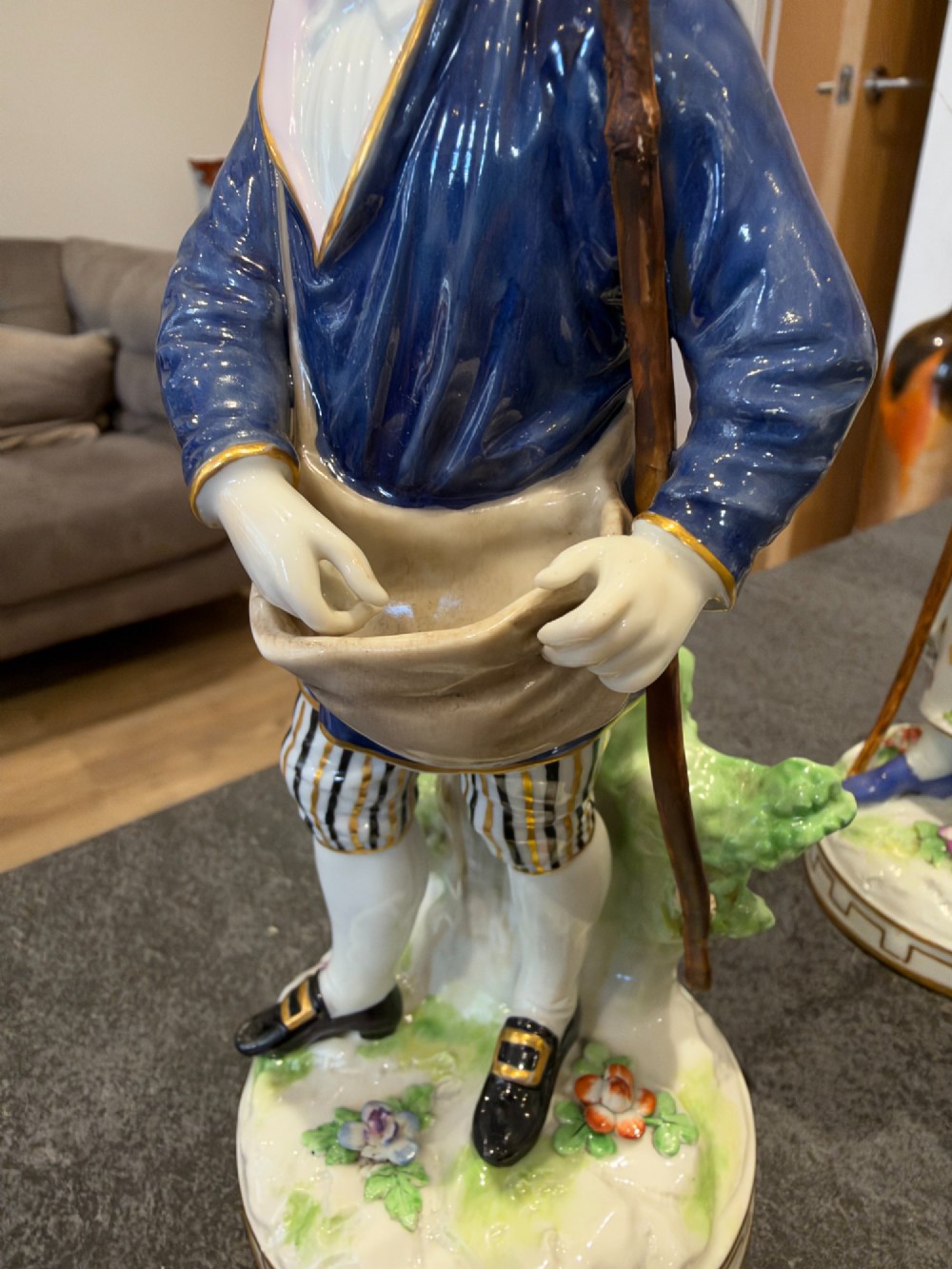 A pair of antique hand-painted German porcelain figures depicting a shepherdess with a lamb and a shepherd holding a basket, set on circular gilded bases. View XIV