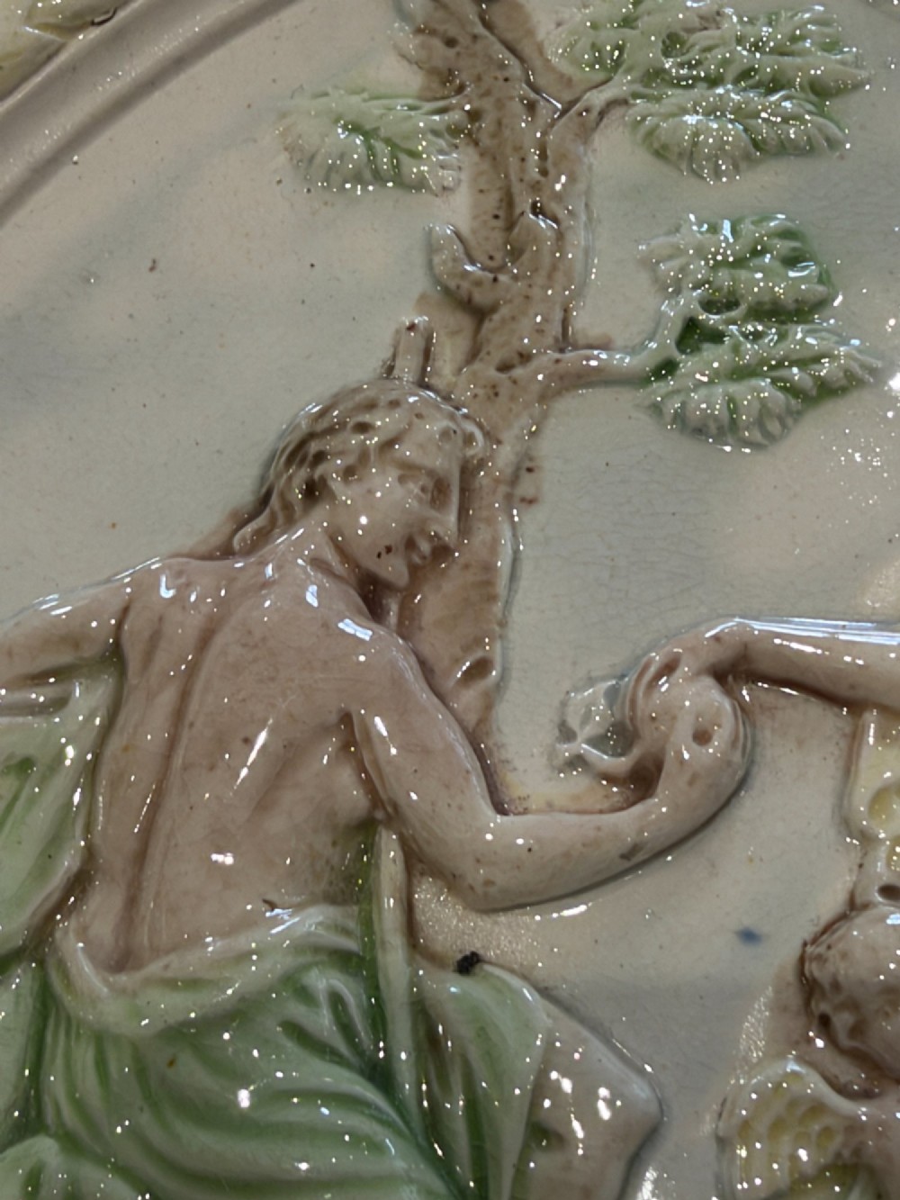 An oval cream and green lead-glazed pearlware plaque featuring relief moulding of classical figures surrounded by an ornate pierced leaf border. View V