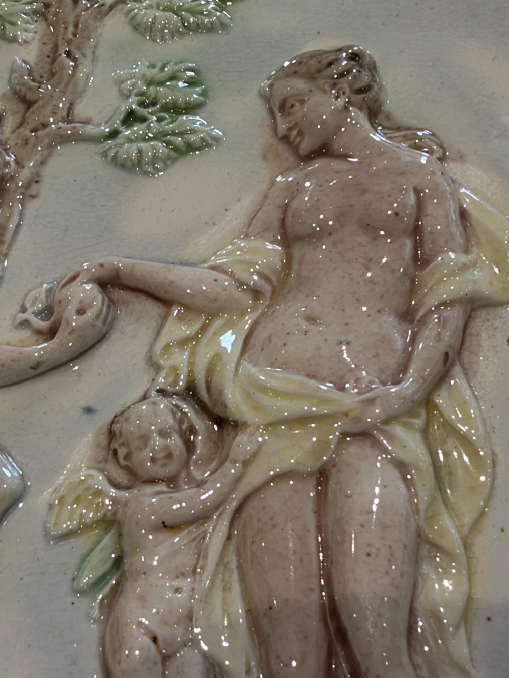 An oval cream and green lead-glazed pearlware plaque featuring relief moulding of classical figures surrounded by an ornate pierced leaf border. View VI