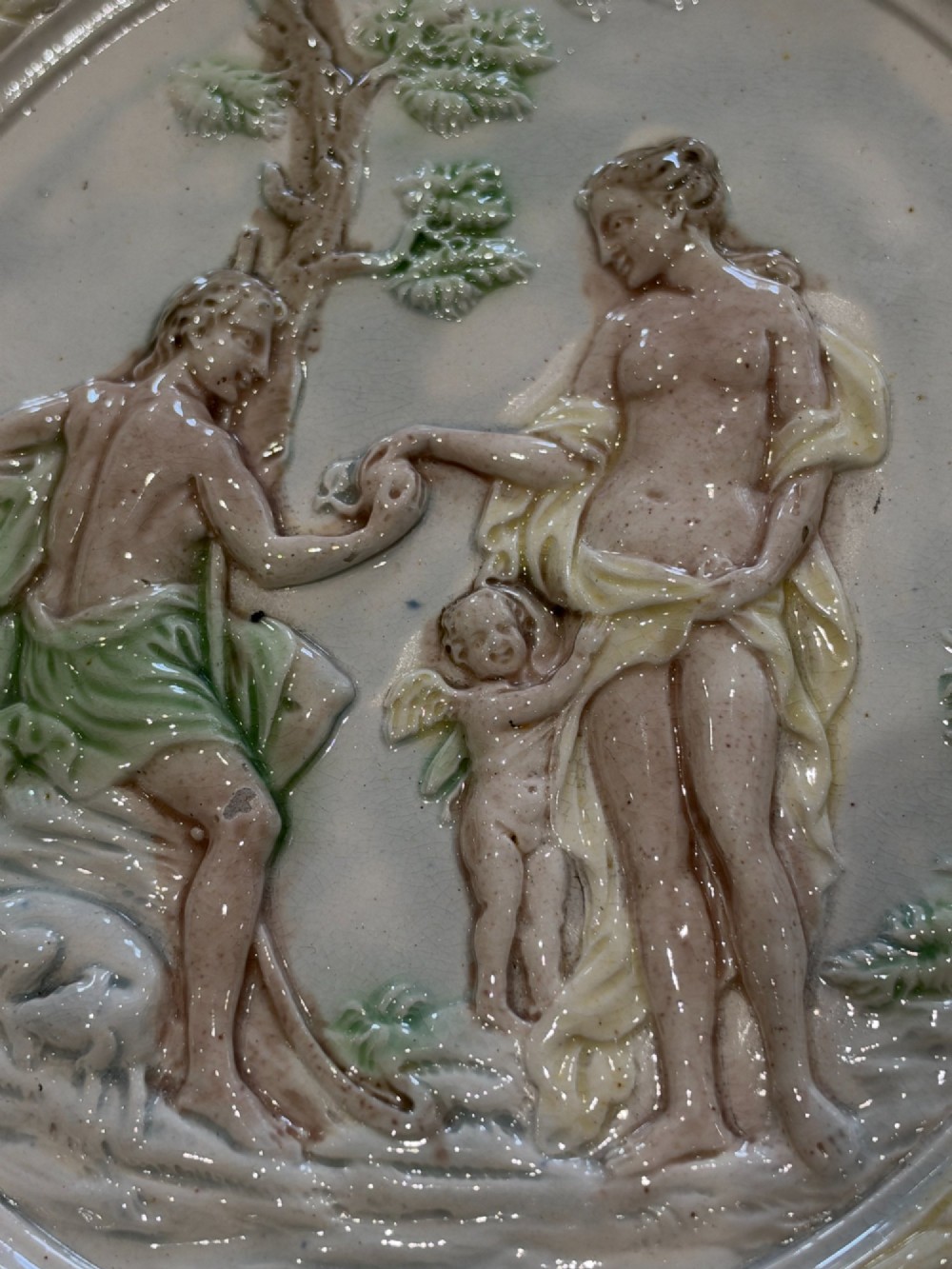 An oval cream and green lead-glazed pearlware plaque featuring relief moulding of classical figures surrounded by an ornate pierced leaf border. View VII