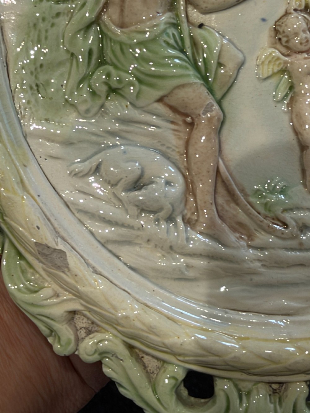 An oval cream and green lead-glazed pearlware plaque featuring relief moulding of classical figures surrounded by an ornate pierced leaf border. View XII