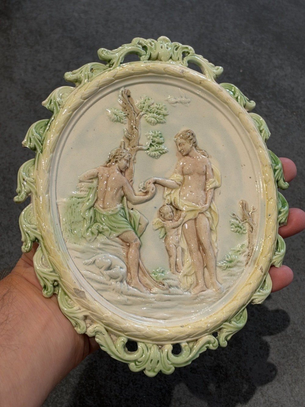 An oval cream and green lead-glazed pearlware plaque featuring relief moulding of classical figures surrounded by an ornate pierced leaf border. View XIV
