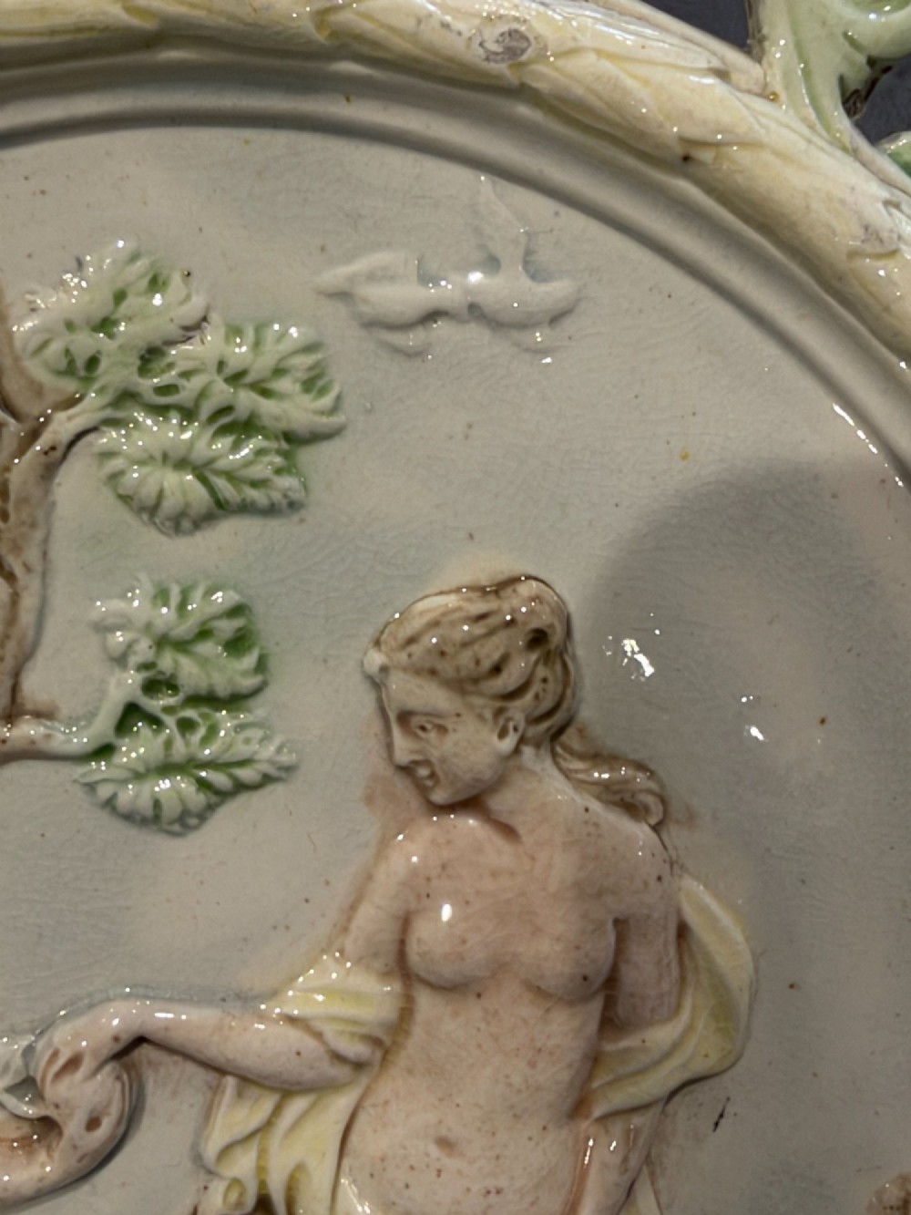 An oval cream and green lead-glazed pearlware plaque featuring relief moulding of classical figures surrounded by an ornate pierced leaf border. View XIII