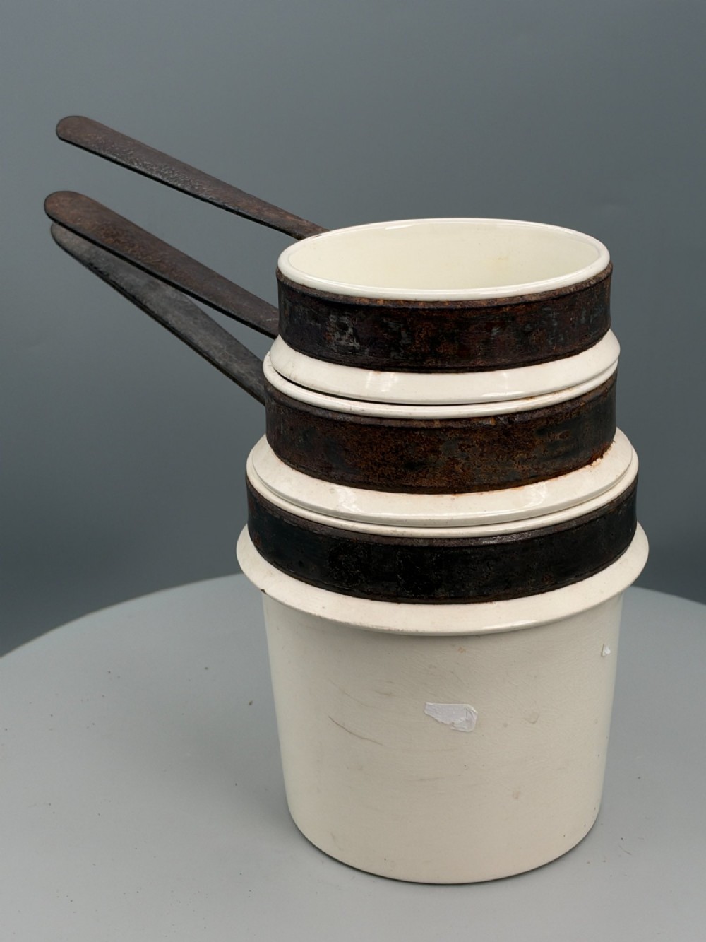 A set of three graduated off-white ceramic cylindrical vessels featuring dark iron bands around the upper rims and extended iron handles. View XIII