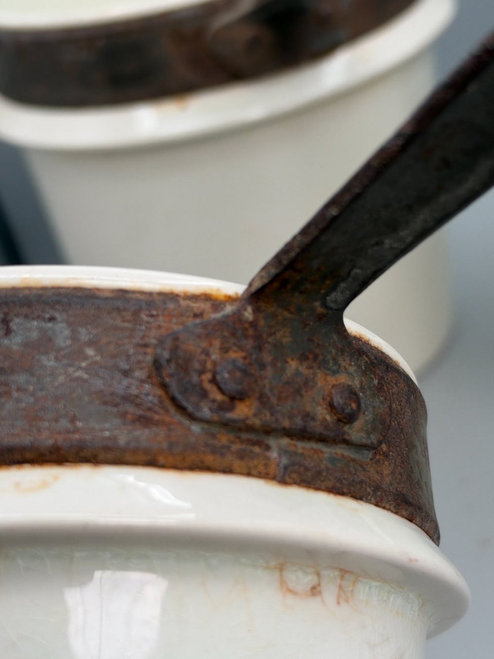 A set of three graduated off-white ceramic cylindrical vessels featuring dark iron bands around the upper rims and extended iron handles. View XIV