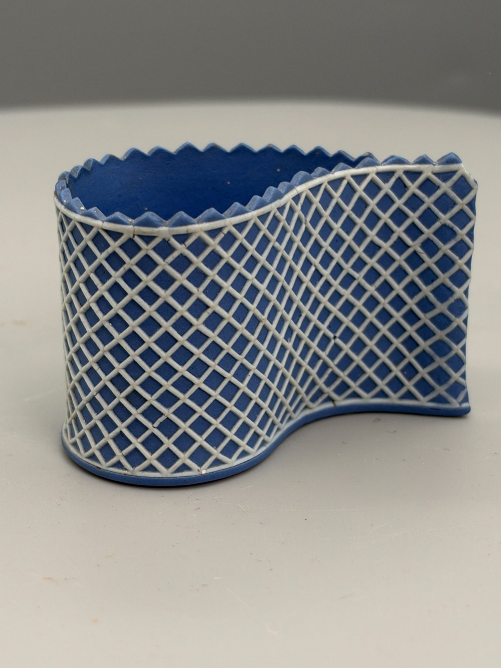 An eighteenth-century curved blue jasperware ceramic vessel decorated with a white lattice pattern and a serrated rim.