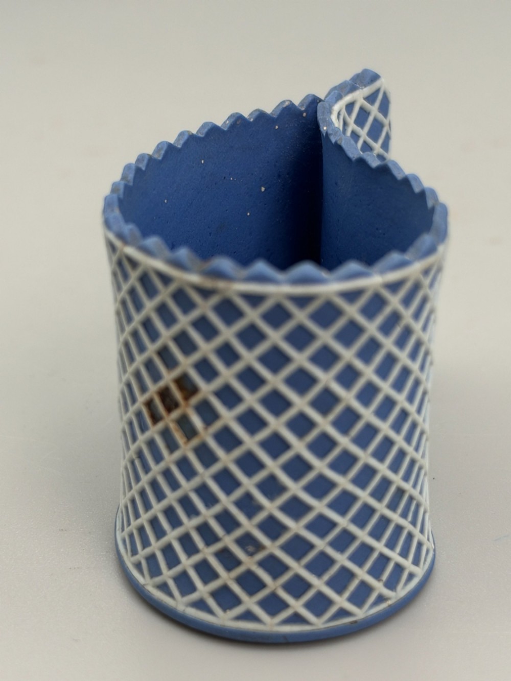 An eighteenth-century curved blue jasperware ceramic vessel decorated with a white lattice pattern and a serrated rim. View II