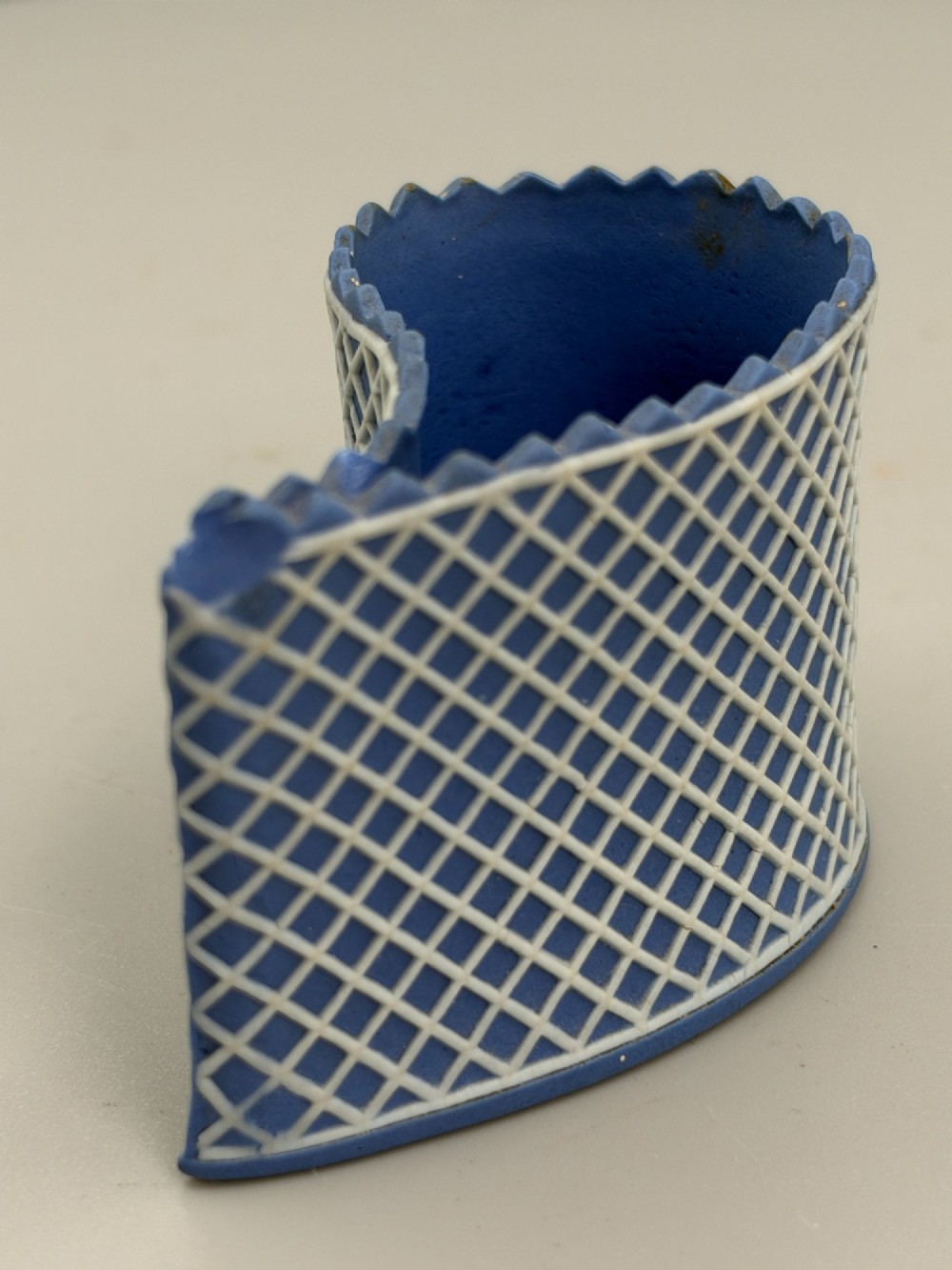 An eighteenth-century curved blue jasperware ceramic vessel decorated with a white lattice pattern and a serrated rim. View IV