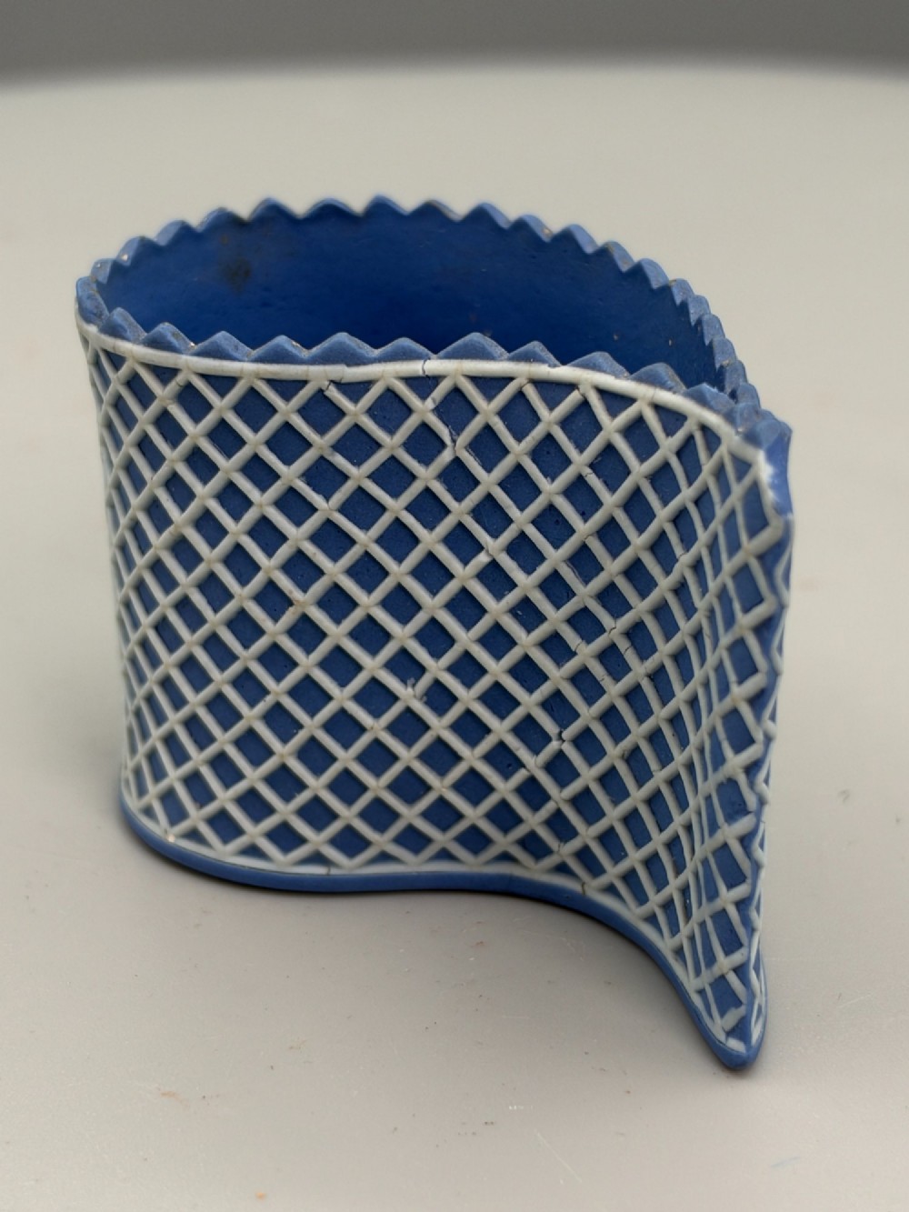 An eighteenth-century curved blue jasperware ceramic vessel decorated with a white lattice pattern and a serrated rim. View V