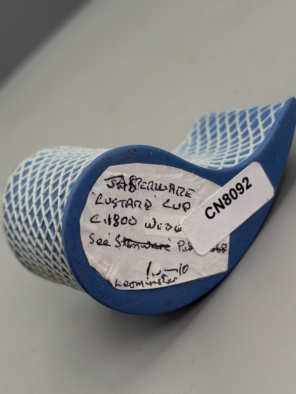 An eighteenth-century curved blue jasperware ceramic vessel decorated with a white lattice pattern and a serrated rim. View X