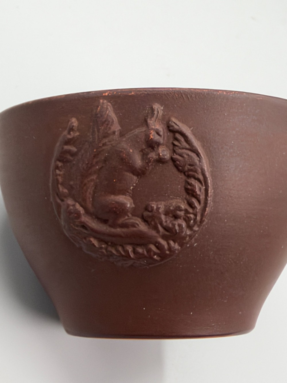 A small reddish-brown Staffordshire red stoneware teacup featuring a loop handle and an applied raised flowerhead sprig motif on its exterior. View II