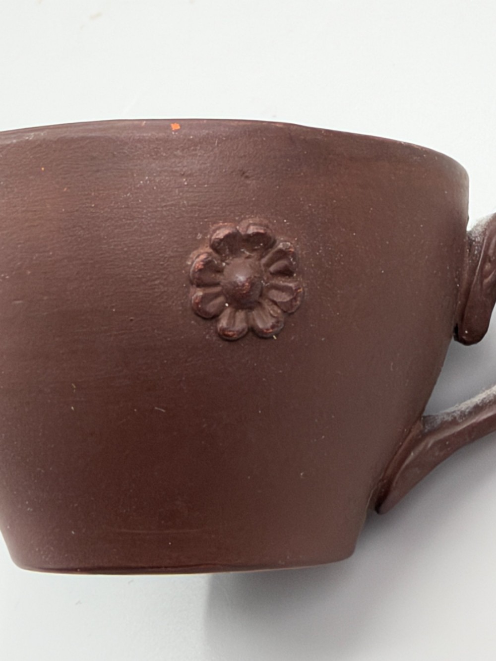 A small reddish-brown Staffordshire red stoneware teacup featuring a loop handle and an applied raised flowerhead sprig motif on its exterior. View IV