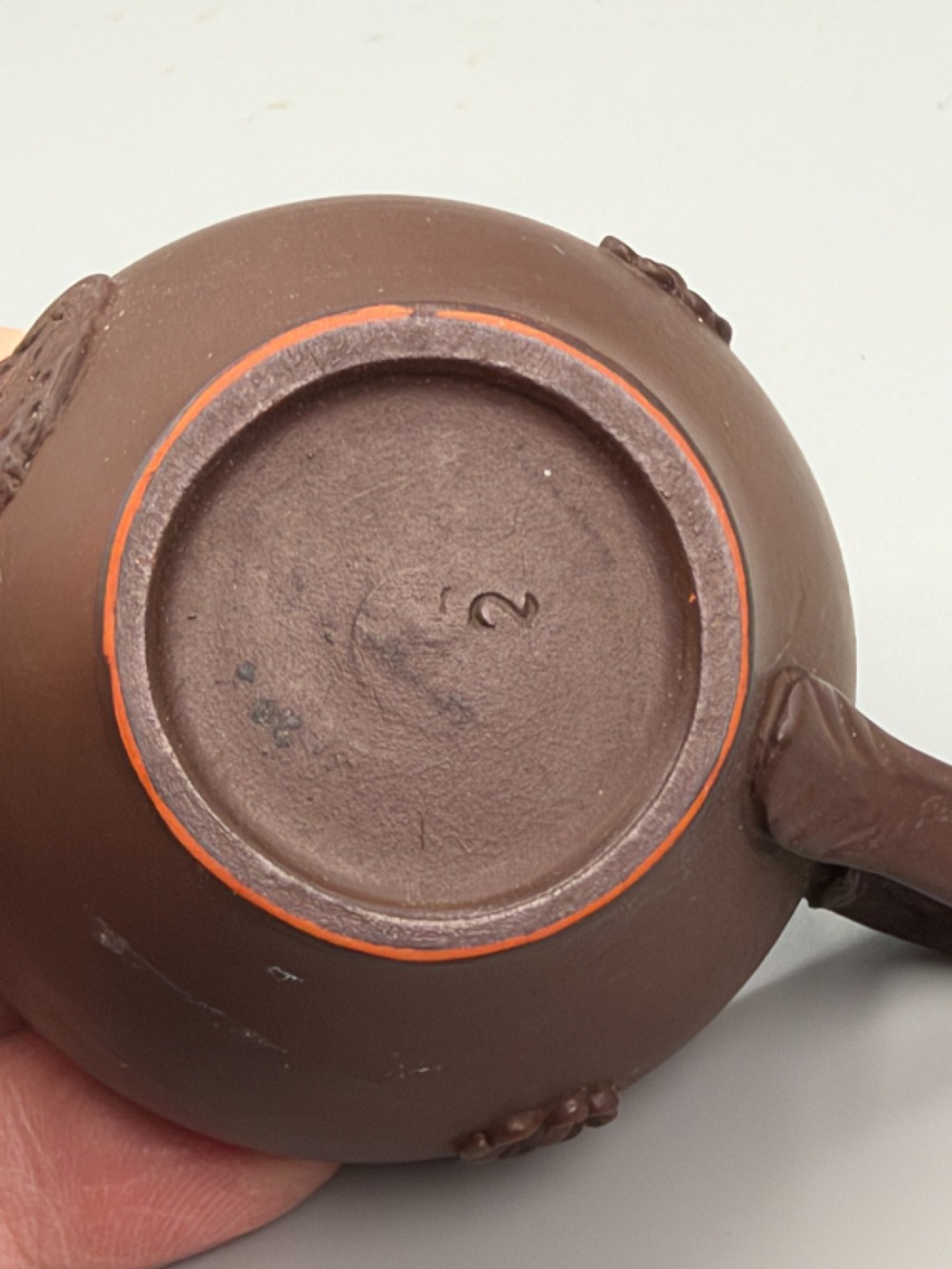 A small reddish-brown Staffordshire red stoneware teacup featuring a loop handle and an applied raised flowerhead sprig motif on its exterior. View V