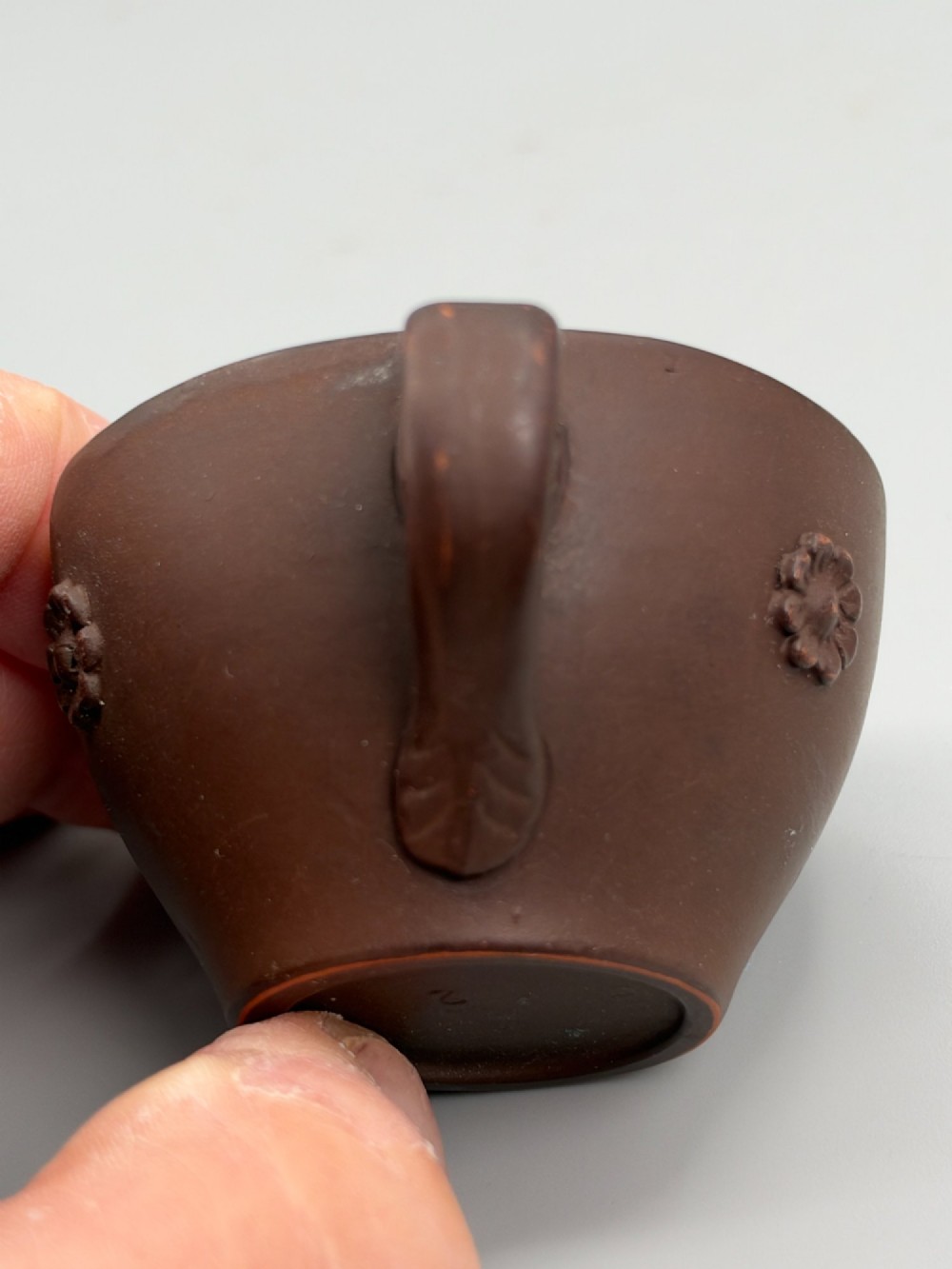 A small reddish-brown Staffordshire red stoneware teacup featuring a loop handle and an applied raised flowerhead sprig motif on its exterior. View VI