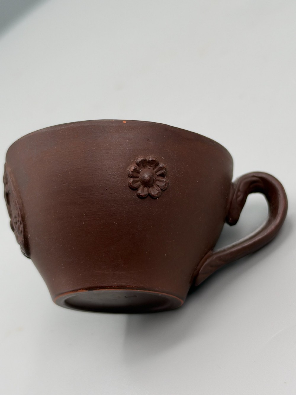 A small reddish-brown Staffordshire red stoneware teacup featuring a loop handle and an applied raised flowerhead sprig motif on its exterior. View VII