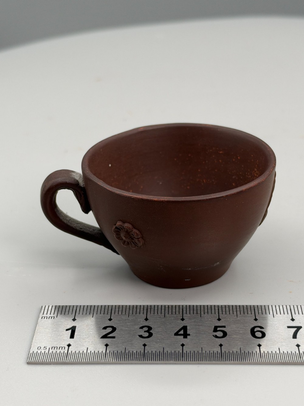 A small reddish-brown Staffordshire red stoneware teacup featuring a loop handle and an applied raised flowerhead sprig motif on its exterior. View VIII