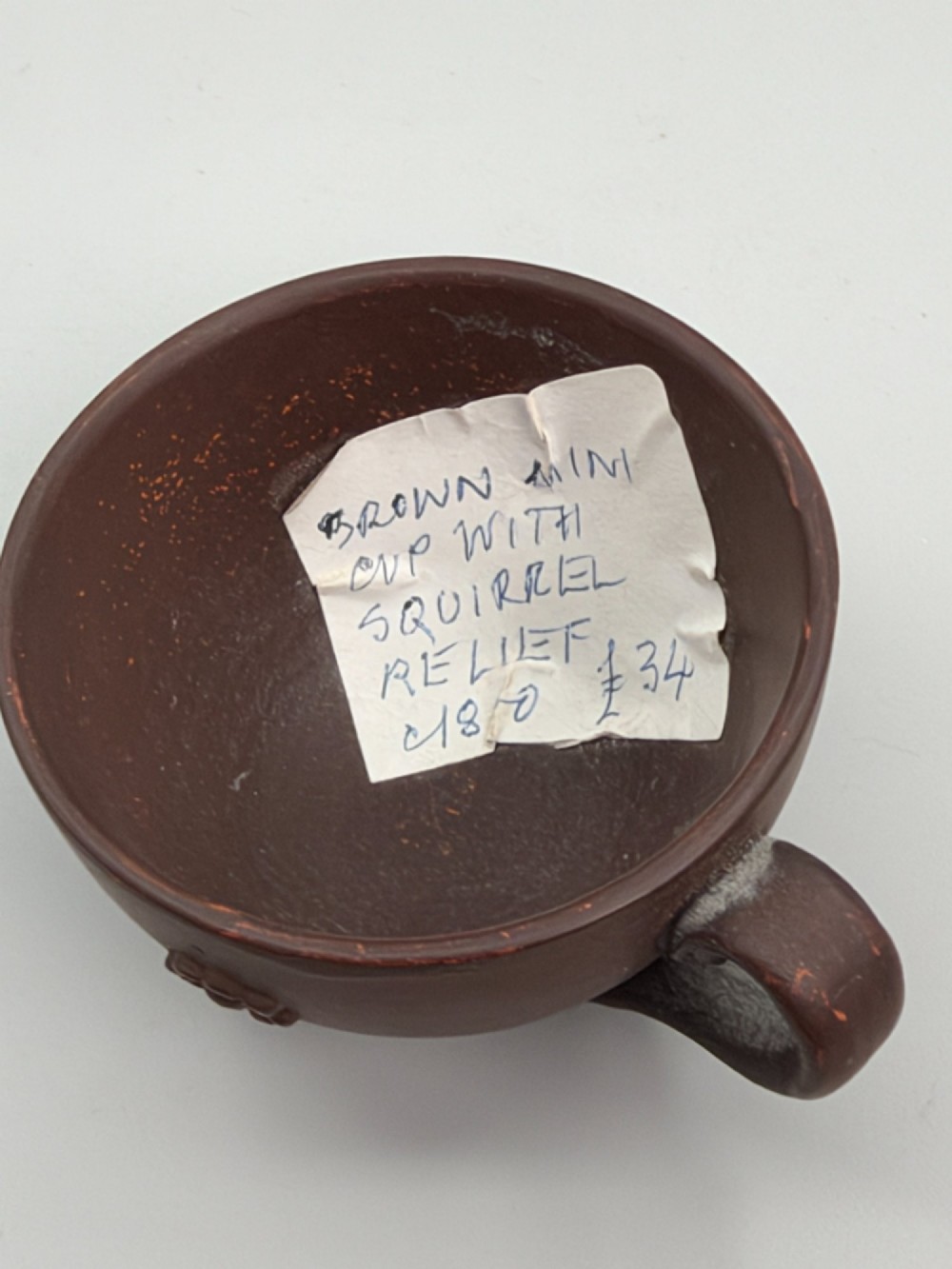 A small reddish-brown Staffordshire red stoneware teacup featuring a loop handle and an applied raised flowerhead sprig motif on its exterior. View IX