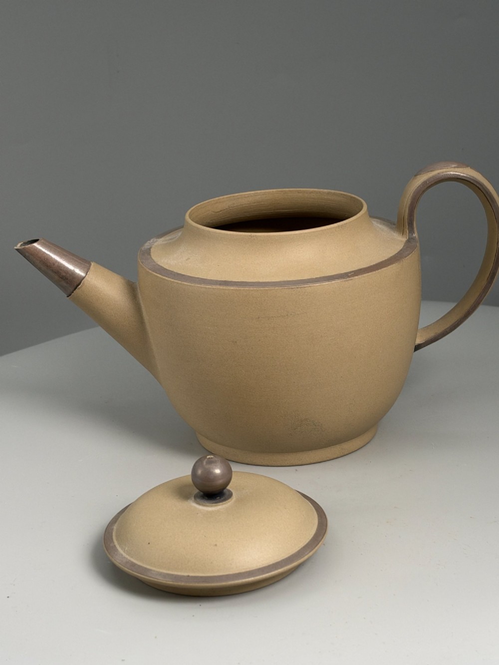 An 18th-century unglazed buff stoneware teapot with dark brown rim bands, a curved handle, and a round lid finial. View III