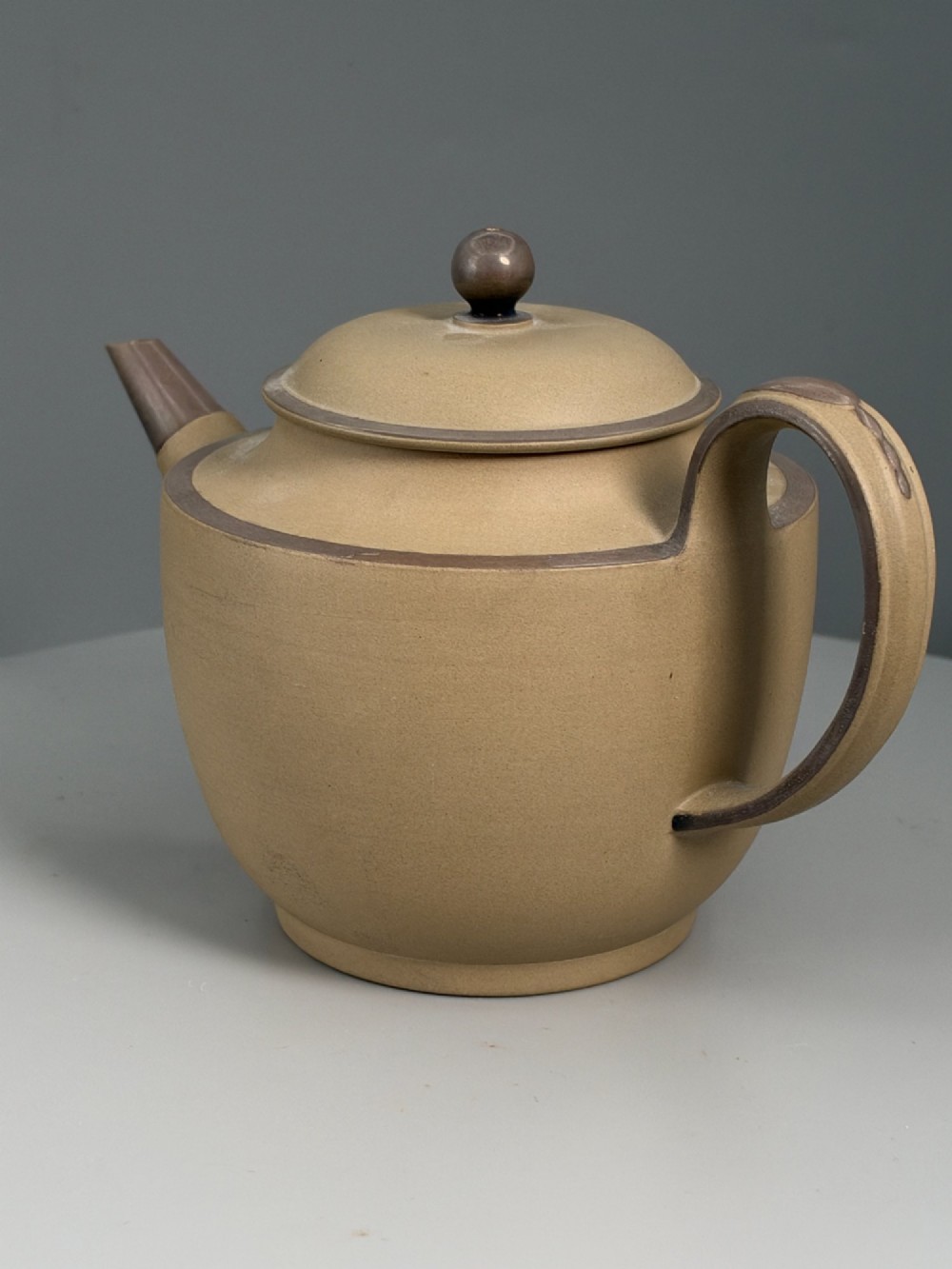 An 18th-century unglazed buff stoneware teapot with dark brown rim bands, a curved handle, and a round lid finial. View IV
