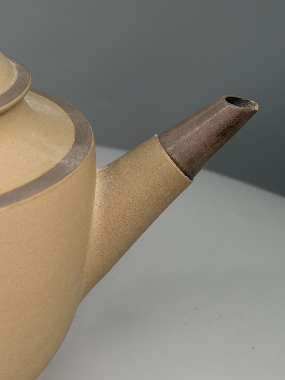 An 18th-century unglazed buff stoneware teapot with dark brown rim bands, a curved handle, and a round lid finial. View VIII