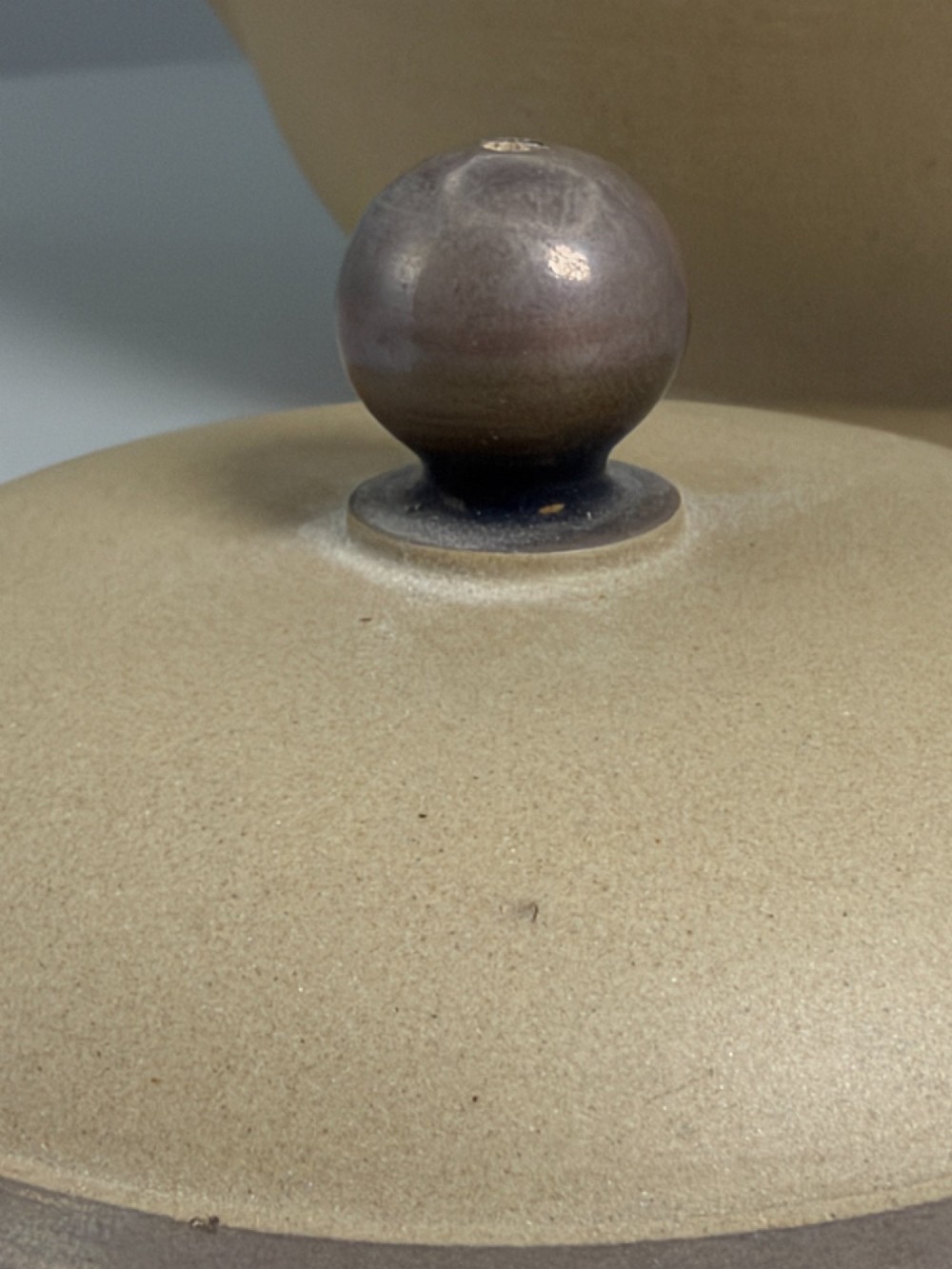 An 18th-century unglazed buff stoneware teapot with dark brown rim bands, a curved handle, and a round lid finial. View XI