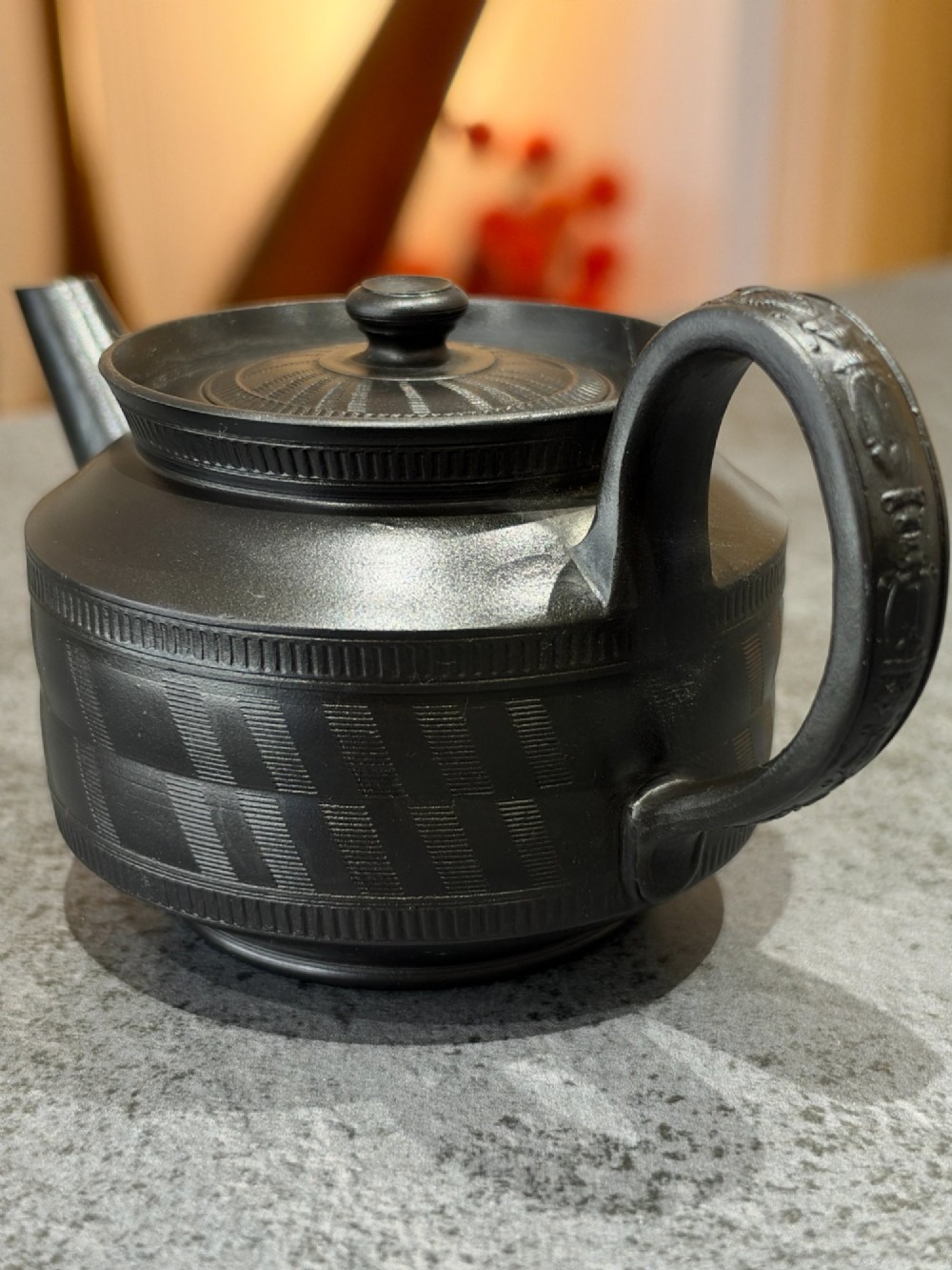 A matte black Georgian basalt stoneware teapot featuring engine-turned geometric band pattern detail and a decorative moulded handle.