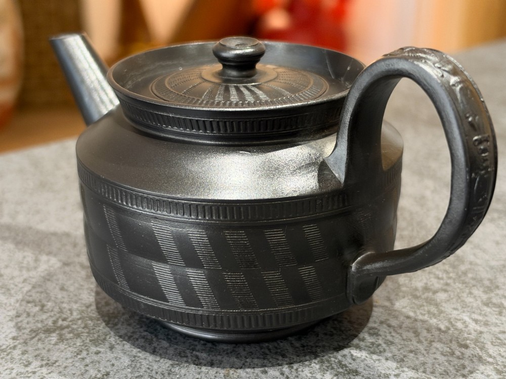 A matte black Georgian basalt stoneware teapot featuring engine-turned geometric band pattern detail and a decorative moulded handle. View X