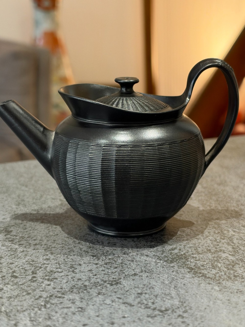 A small Georgian black basalt ware teapot featuring a ribbed pattern on the lower body, an arched handle, and a matching lid with a knob finial.
