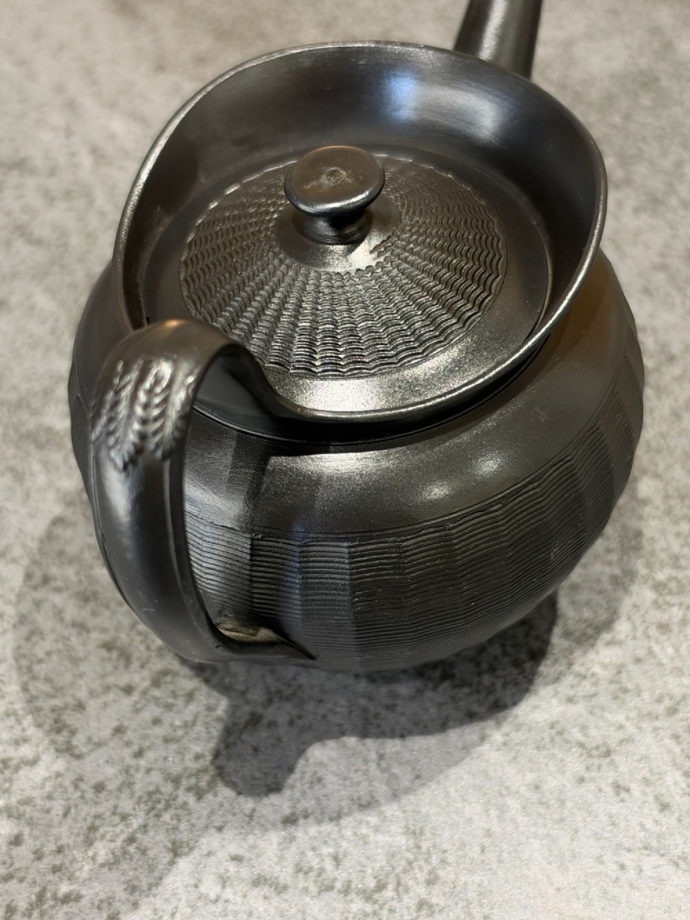 A small Georgian black basalt ware teapot featuring a ribbed pattern on the lower body, an arched handle, and a matching lid with a knob finial. View V