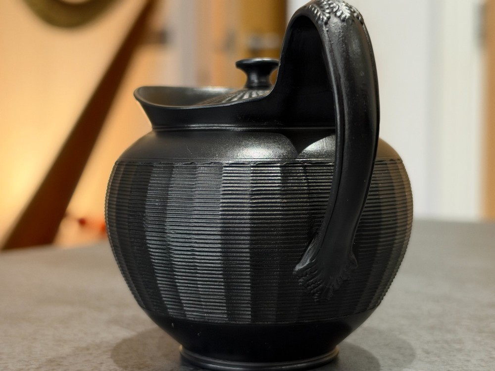 A small Georgian black basalt ware teapot featuring a ribbed pattern on the lower body, an arched handle, and a matching lid with a knob finial. View VI