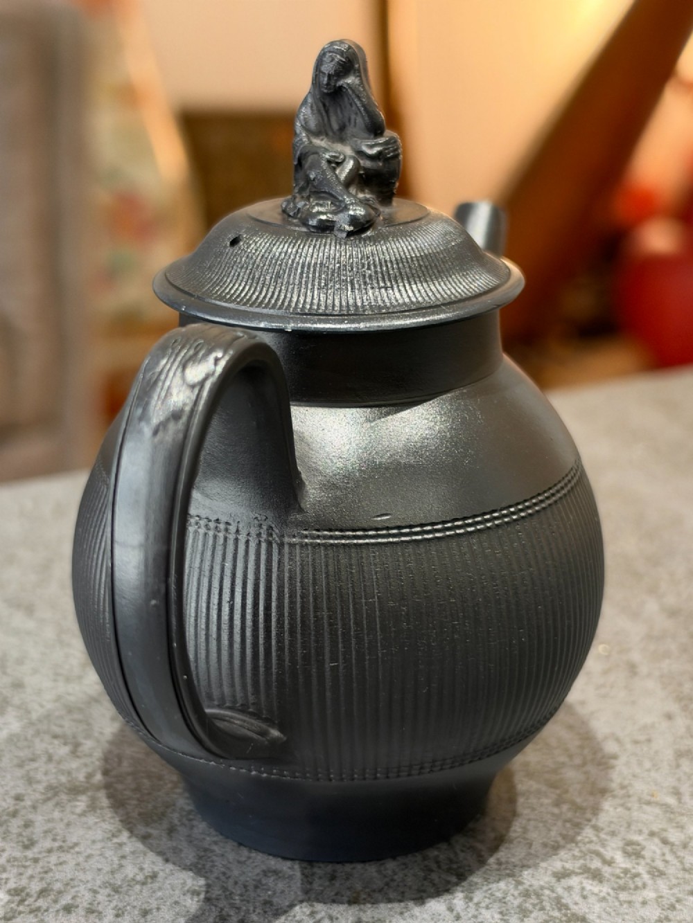 An antique matte black basalt teapot featuring an engine-turned ribbed body, a fitted lid with a figural knop, and a curved handle. View II
