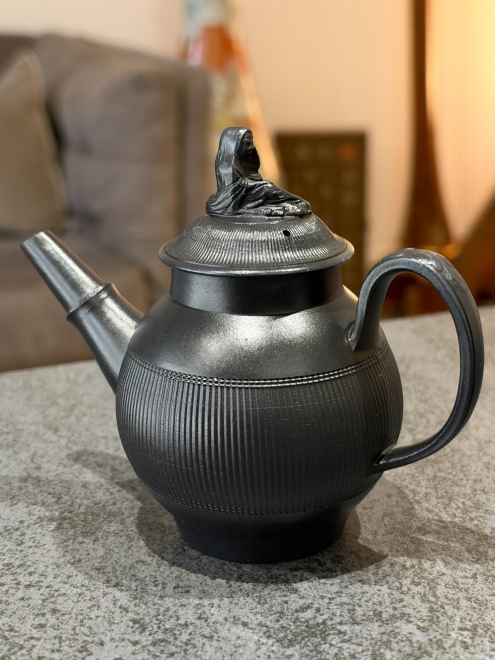An antique matte black basalt teapot featuring an engine-turned ribbed body, a fitted lid with a figural knop, and a curved handle. View III