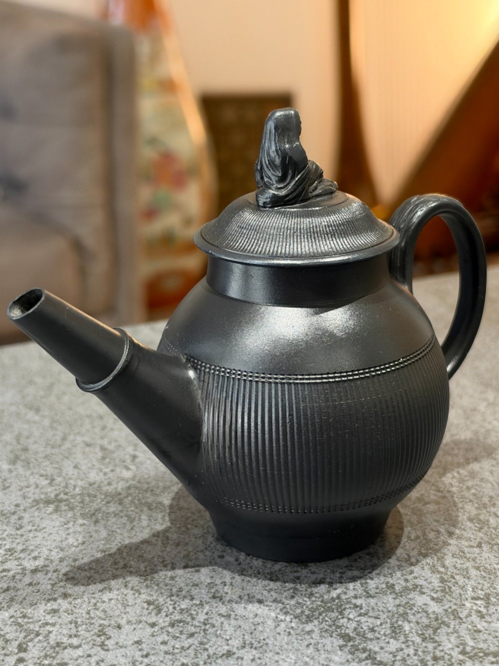 An antique matte black basalt teapot featuring an engine-turned ribbed body, a fitted lid with a figural knop, and a curved handle. View IV