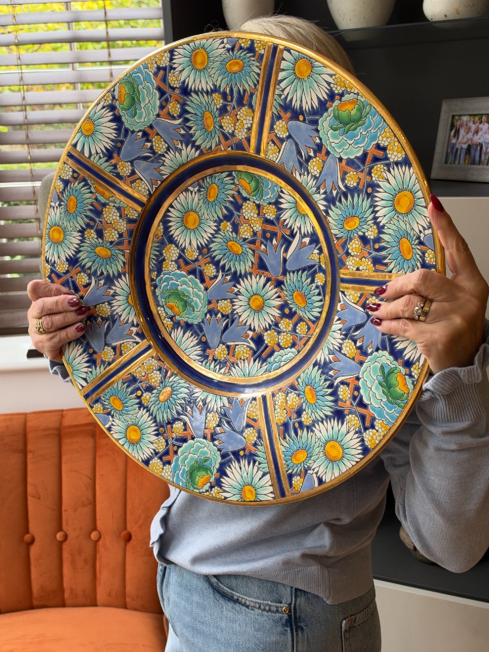 A circular Art Deco ceramic charger featuring radial segmented panels decorated with blue, turquoise, yellow, and white floral enamel patterns bordered in gold. View II