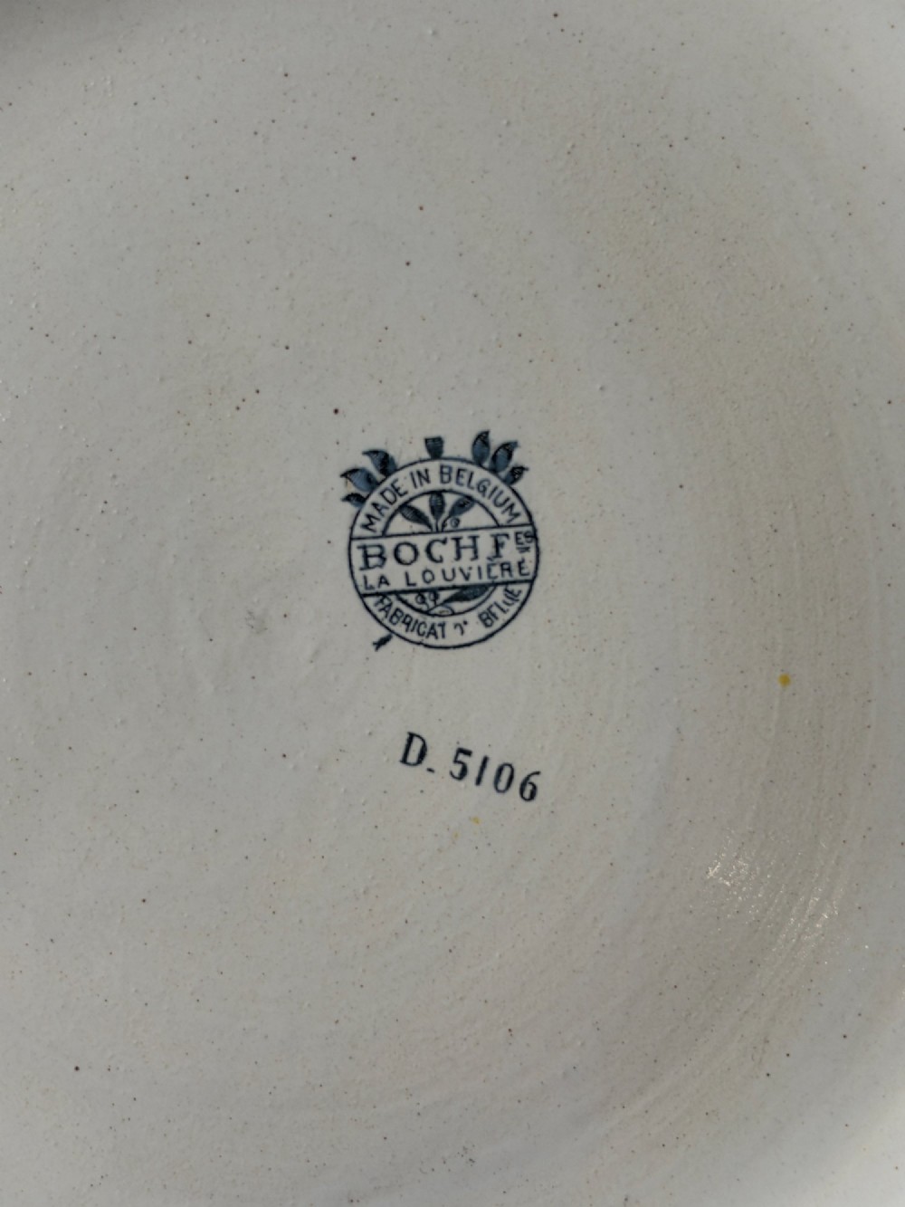 A circular Art Deco ceramic charger featuring radial segmented panels decorated with blue, turquoise, yellow, and white floral enamel patterns bordered in gold. View VII