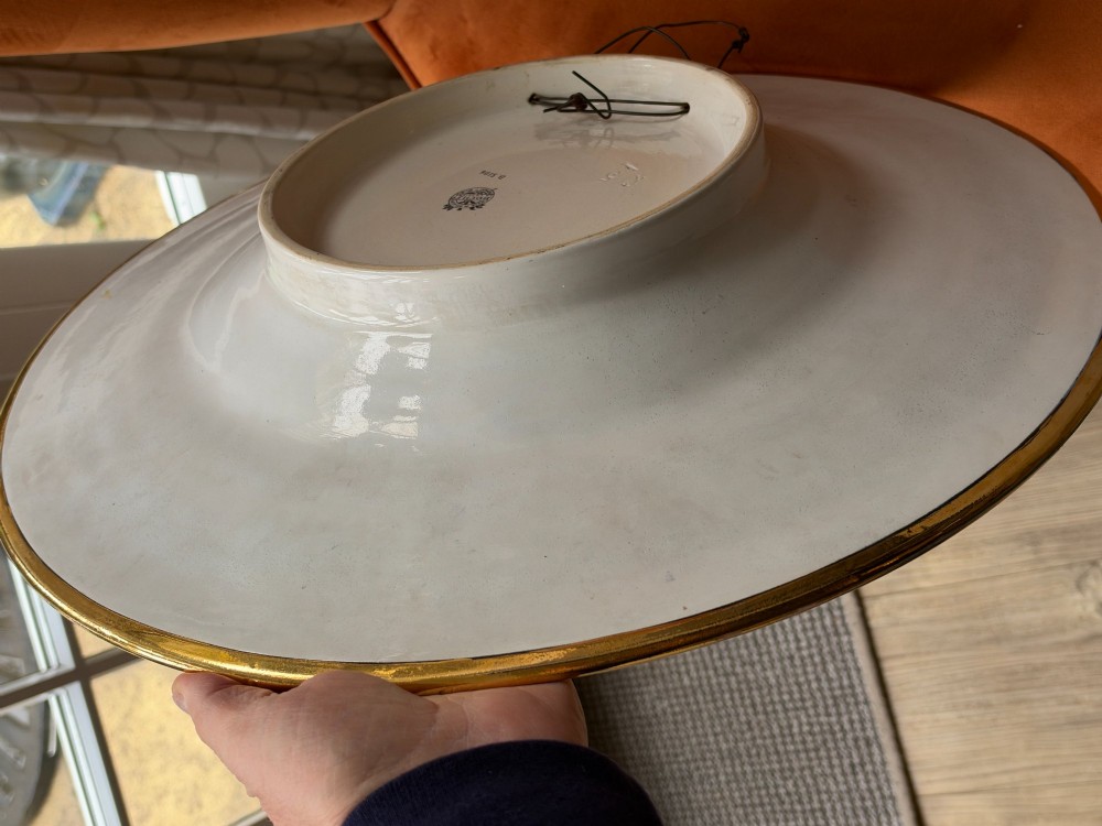 A circular Art Deco ceramic charger featuring radial segmented panels decorated with blue, turquoise, yellow, and white floral enamel patterns bordered in gold. View VIII