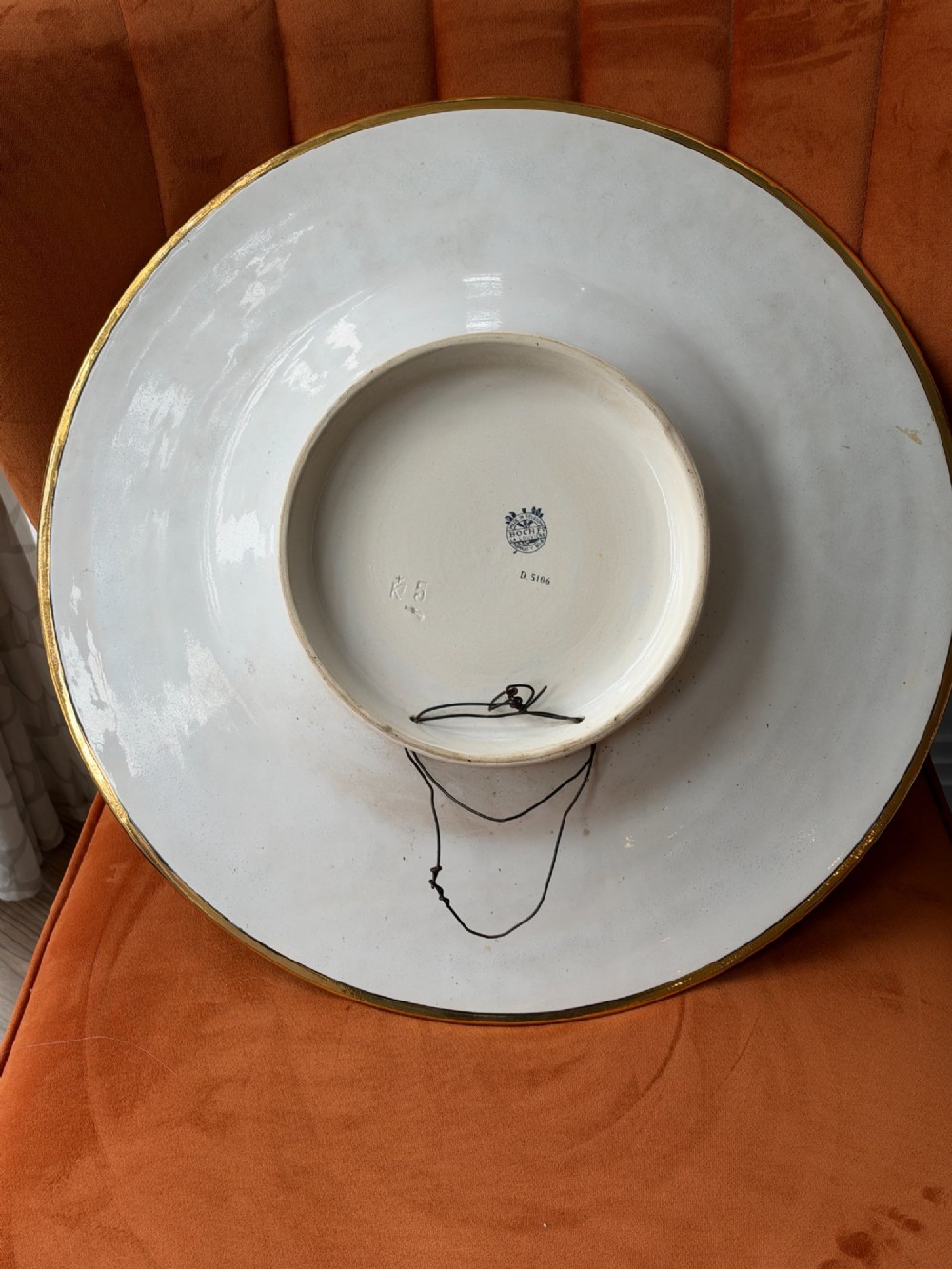 A circular Art Deco ceramic charger featuring radial segmented panels decorated with blue, turquoise, yellow, and white floral enamel patterns bordered in gold. View X