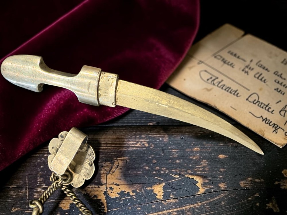 An antique Caucasian curved silver miniature dagger brooch featuring black niello scrollwork motifs and an attached suspension chain with a matching circular clasp. View VIII