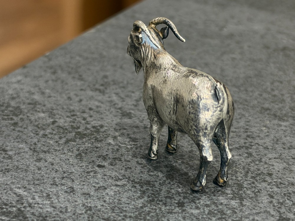 A small cast sterling silver miniature figurine of a billy goat displaying detailed fur texture, curved horns, and British hallmarks stamped along its side. View III
