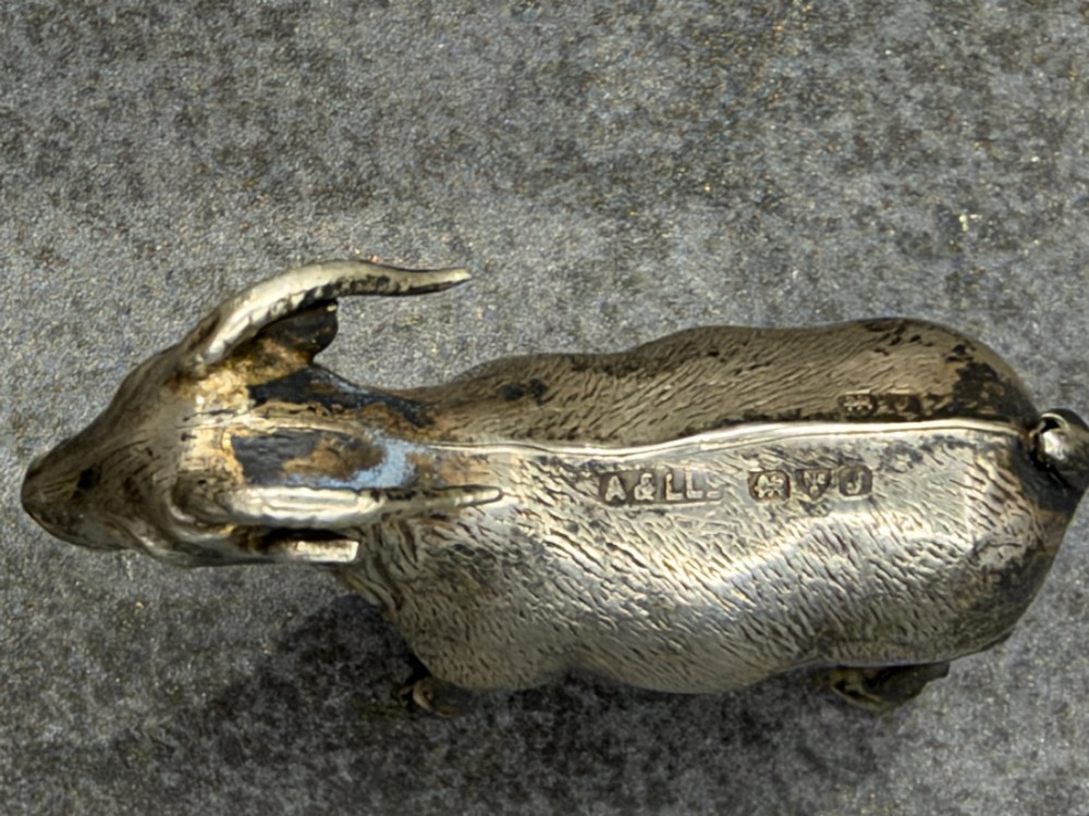 A small cast sterling silver miniature figurine of a billy goat displaying detailed fur texture, curved horns, and British hallmarks stamped along its side. View IV