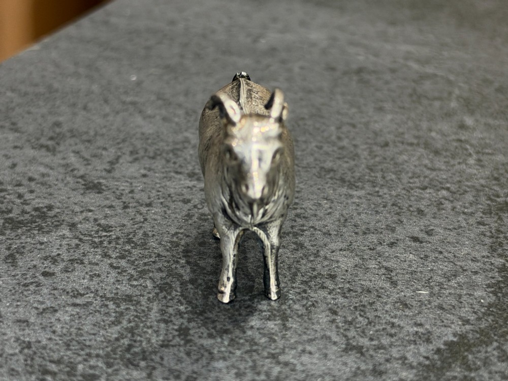A small cast sterling silver miniature figurine of a billy goat displaying detailed fur texture, curved horns, and British hallmarks stamped along its side. View V