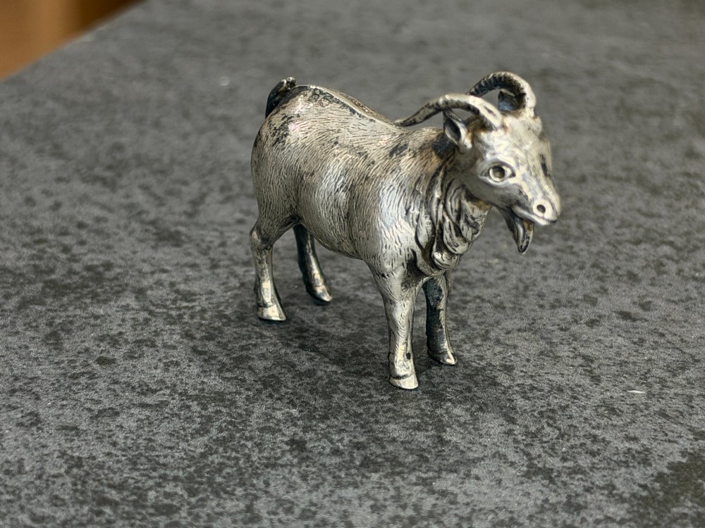 A small cast sterling silver miniature figurine of a billy goat displaying detailed fur texture, curved horns, and British hallmarks stamped along its side. View VI