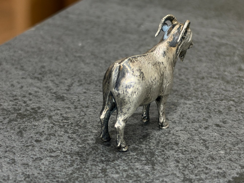 A small cast sterling silver miniature figurine of a billy goat displaying detailed fur texture, curved horns, and British hallmarks stamped along its side. View VII