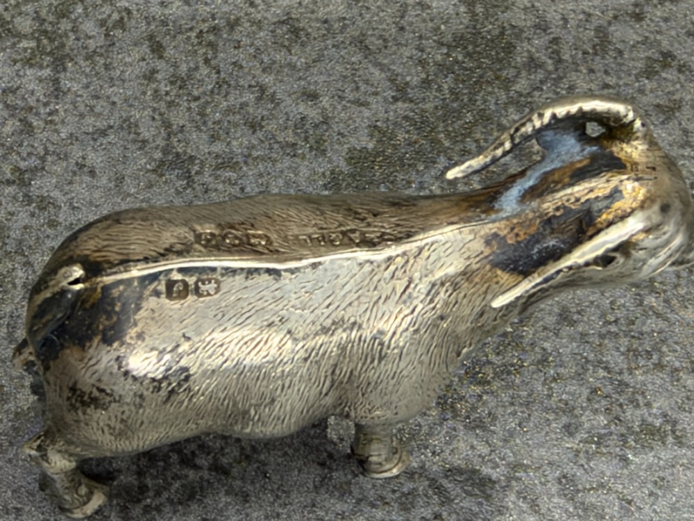 A small cast sterling silver miniature figurine of a billy goat displaying detailed fur texture, curved horns, and British hallmarks stamped along its side. View VIII