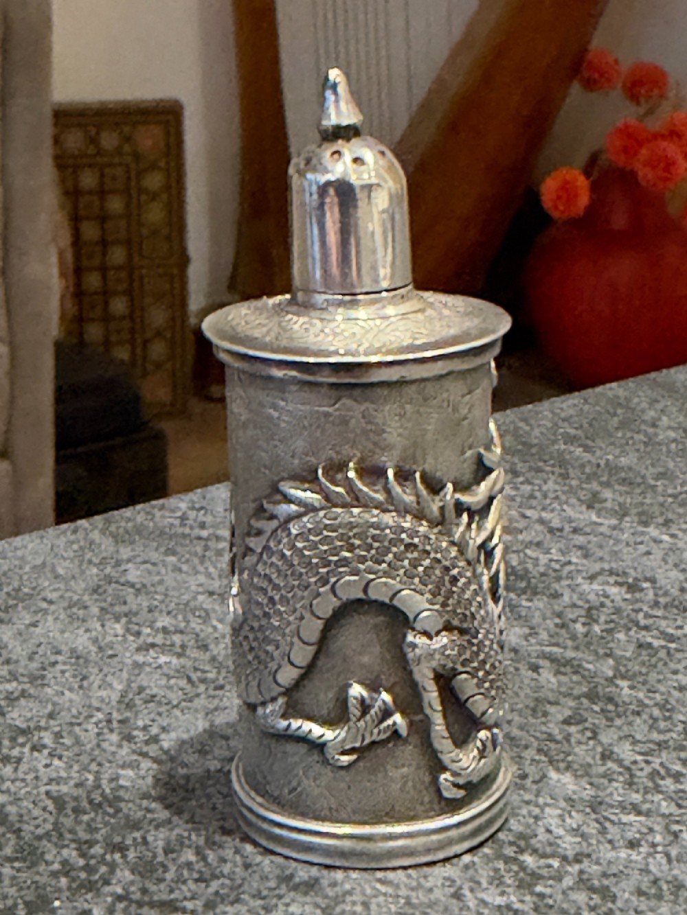 A cylindrical silver pepper shaker decorated with a detailed dragon repousse motif against a textured background with a pointed finial cap. View VII