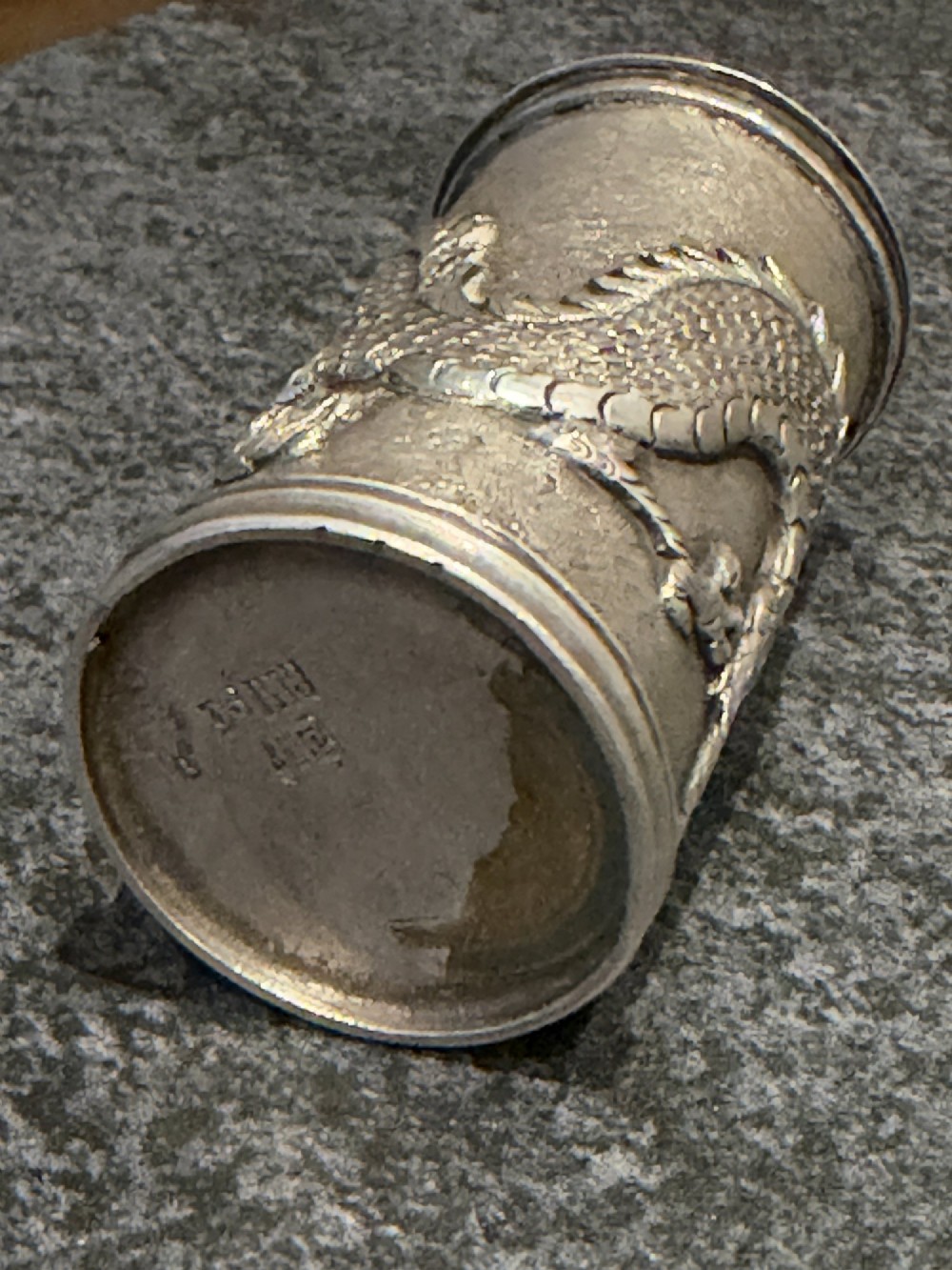 A cylindrical silver pepper shaker decorated with a detailed dragon repousse motif against a textured background with a pointed finial cap. View IX