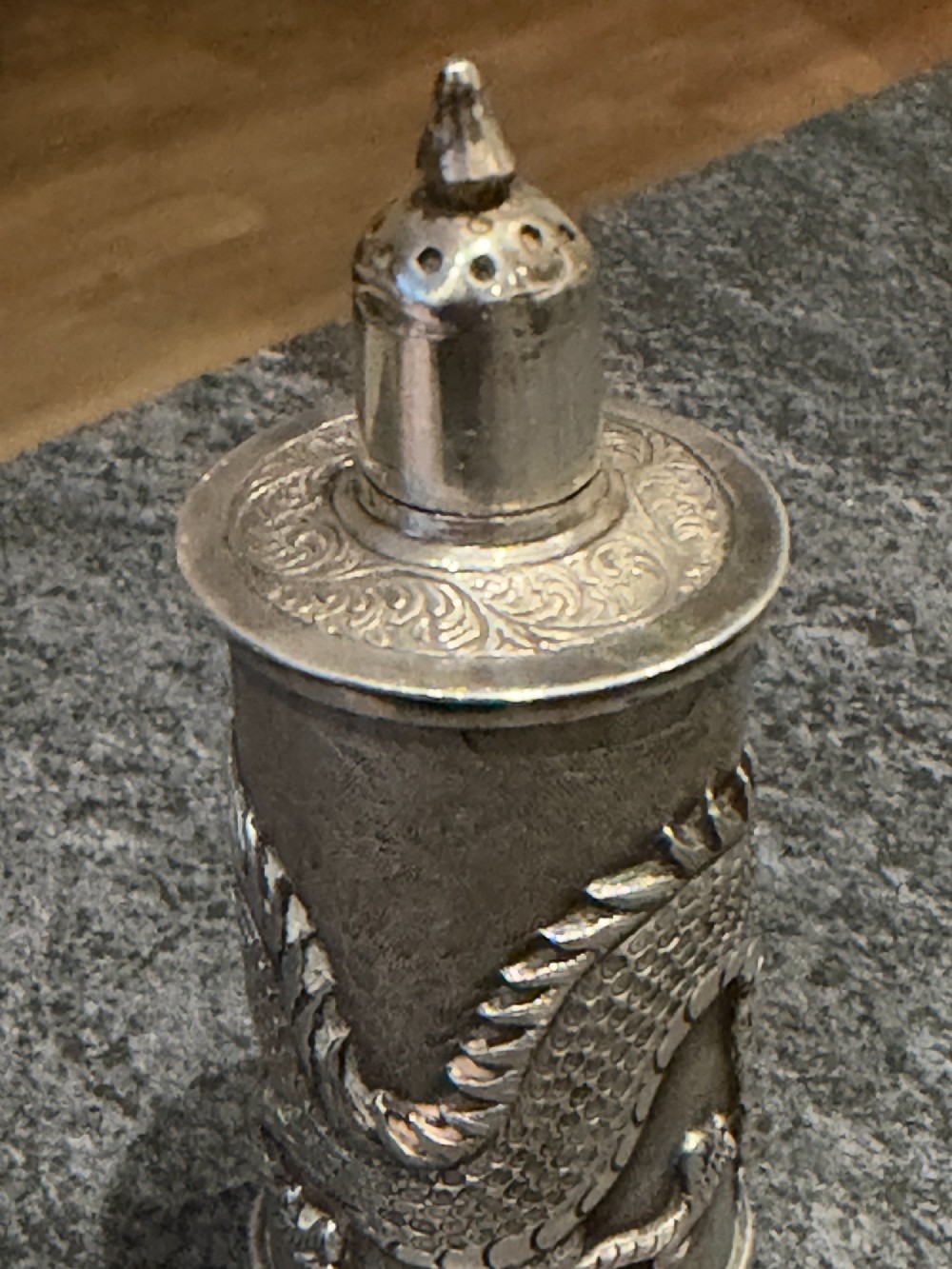 A cylindrical silver pepper shaker decorated with a detailed dragon repousse motif against a textured background with a pointed finial cap. View XI