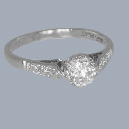 fig 2. An Art Deco diamond solitaire ring featuring a round central diamond flanked by geometric shoulders set with small accent diamonds in white gold and platinum.