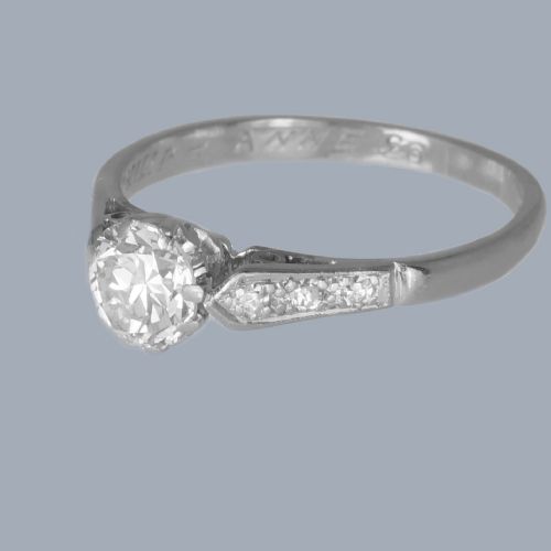 fig 3. An Art Deco diamond solitaire ring featuring a round central diamond flanked by geometric shoulders set with small accent diamonds in white gold and platinum.